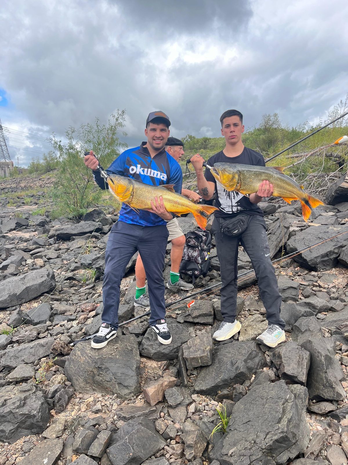 Dos pescadores mostrando dos dorados grandes en la costa